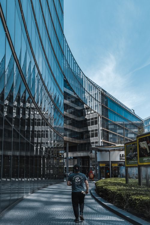 Free Man walking by modern glass architecture in Berlin during daytime. Stock Photo