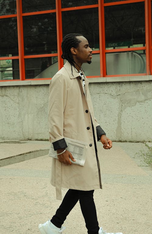 A man in a trench coat and sneakers walking down the street