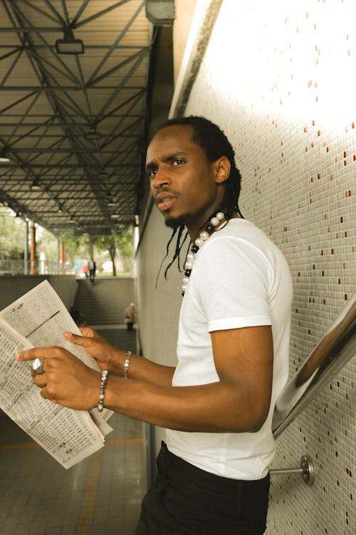 A man with dreadlocks is reading a newspaper