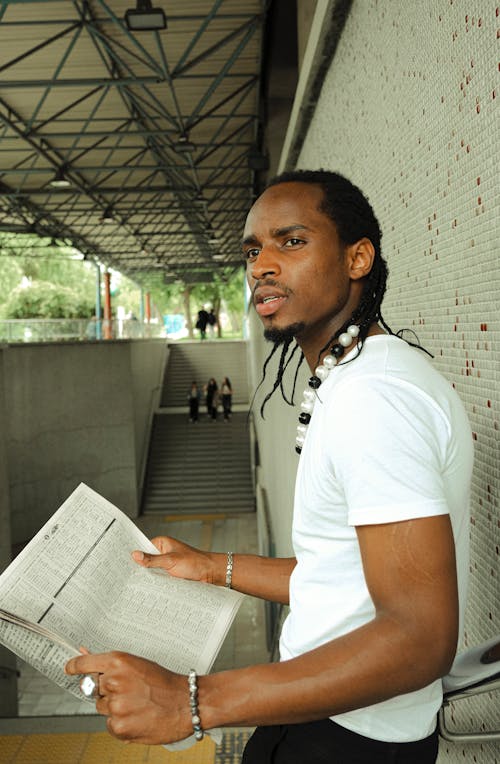 A man with dreadlocks is reading a newspaper