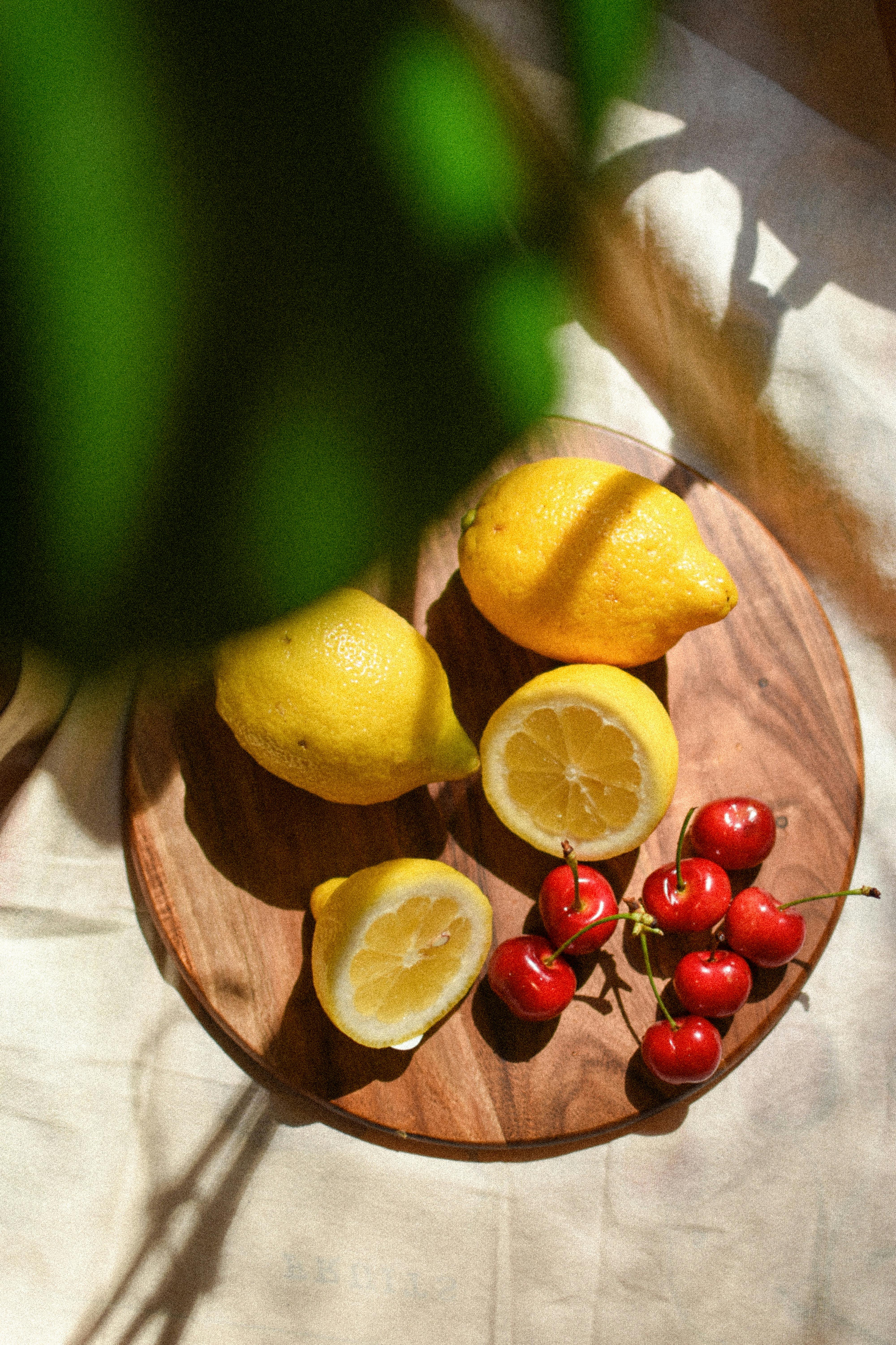 Sunlit lemons and cherries arranged on a wooden cutting board, showcasing vibrant fruit colors.