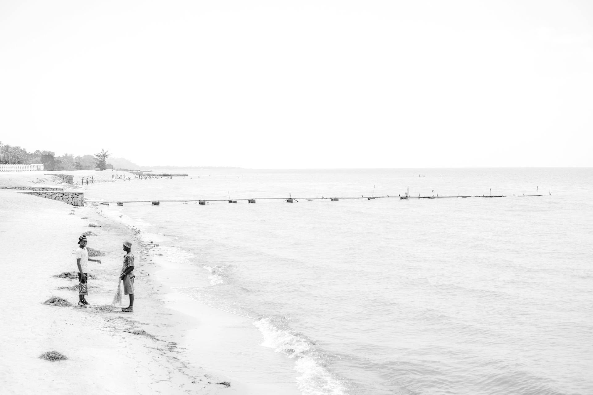 Two fishermen gathering nets on the serene shores of Lake Malawi in a monochrome setting.