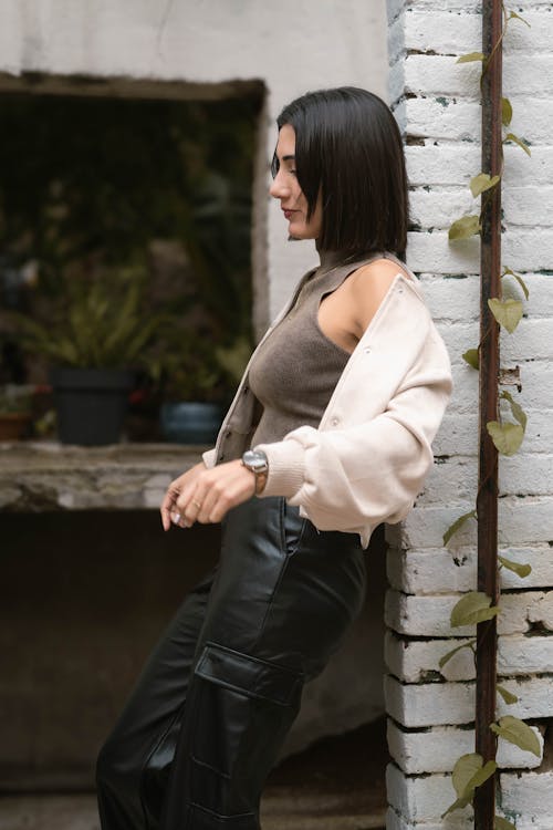 A woman in leather pants leaning against a brick wall