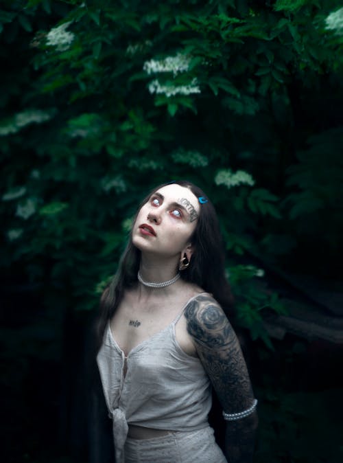 A woman with tattoos and piercings standing in the woods