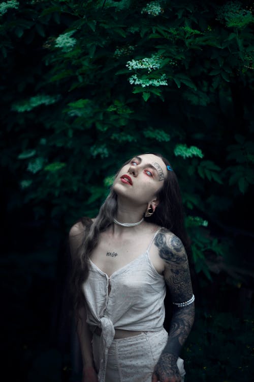 A woman with tattoos and a dress standing in the woods