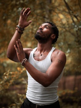 A thoughtful man in a white tank top connects with nature in a serene forest setting.