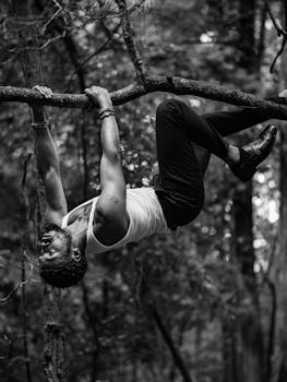 A black and white photo of a man hanging from a tree branch in a forest.