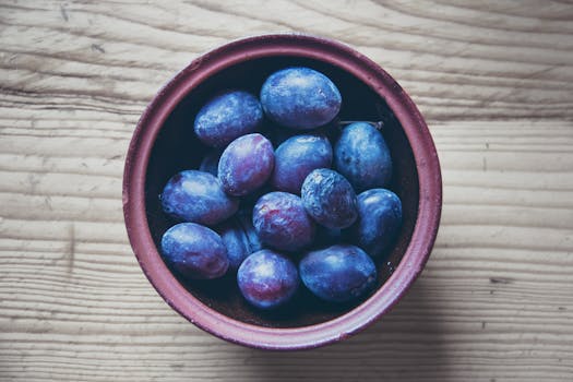 Top view of fresh organic plums in a rustic bowl on a wooden table, perfect for healthy diet themes.