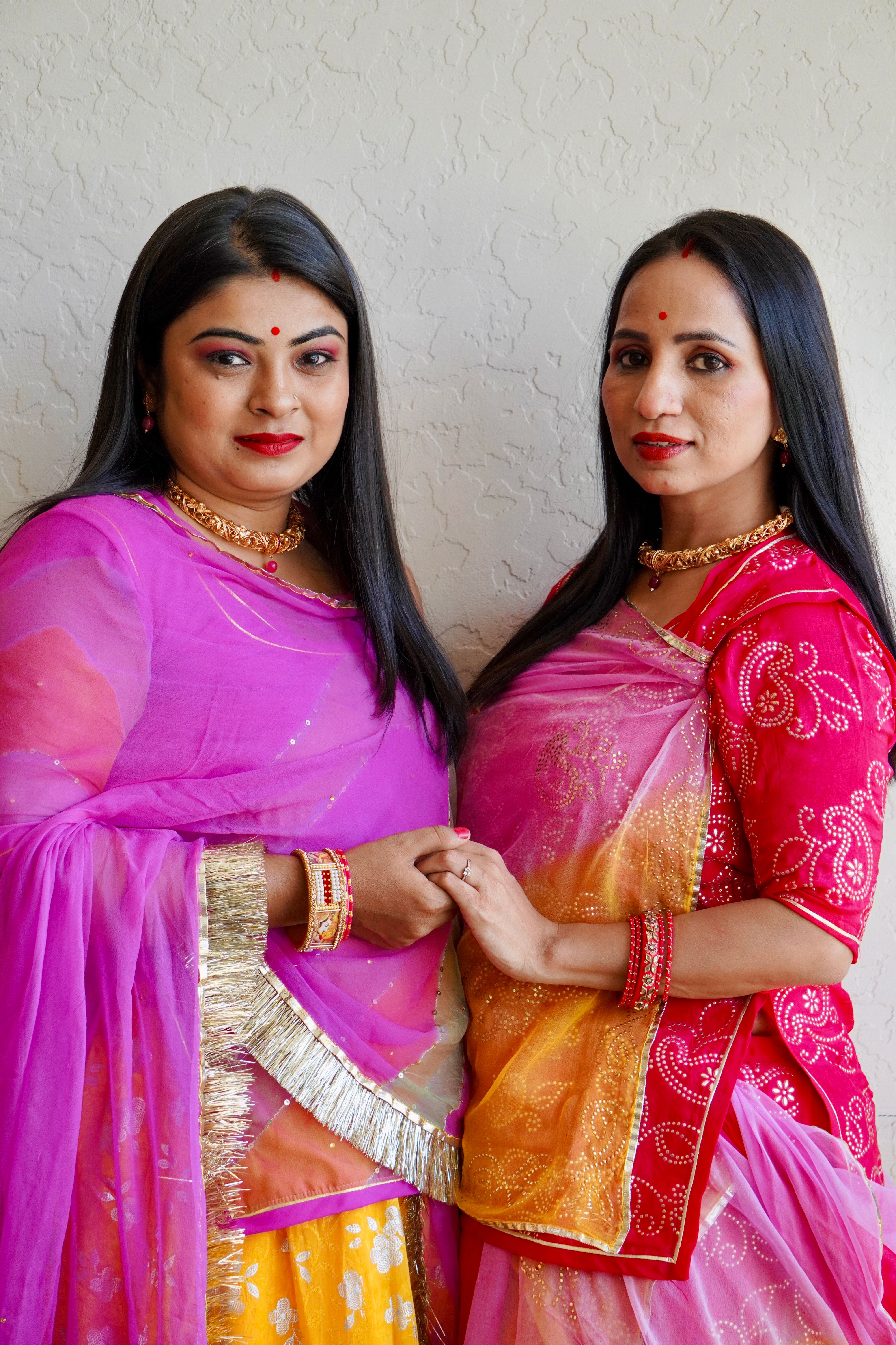 Two Indian women in colorful sari dresses, smiling and posing indoors.