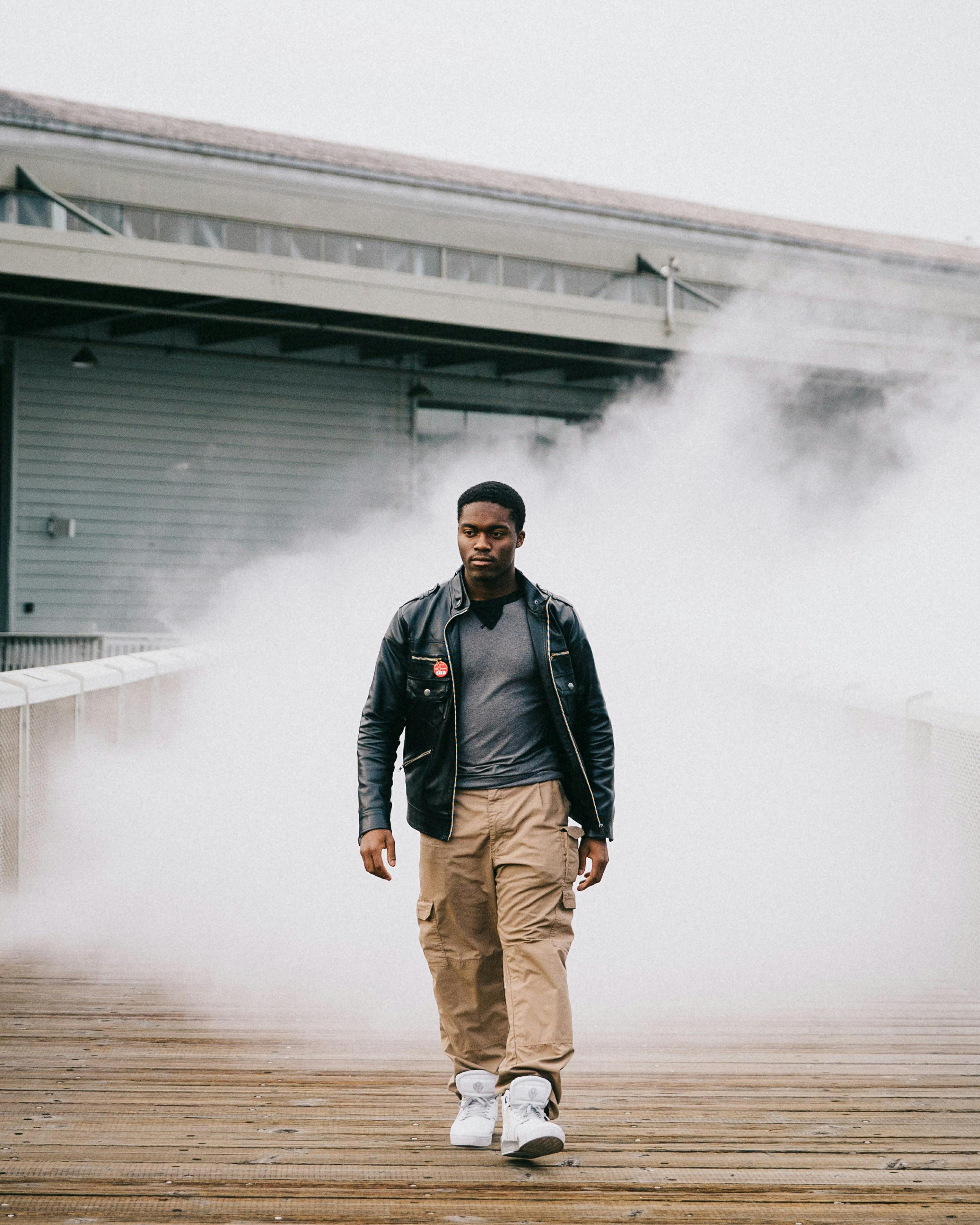 一个穿着皮夹克的男人，自信地走在雾蒙蒙的城市街道上