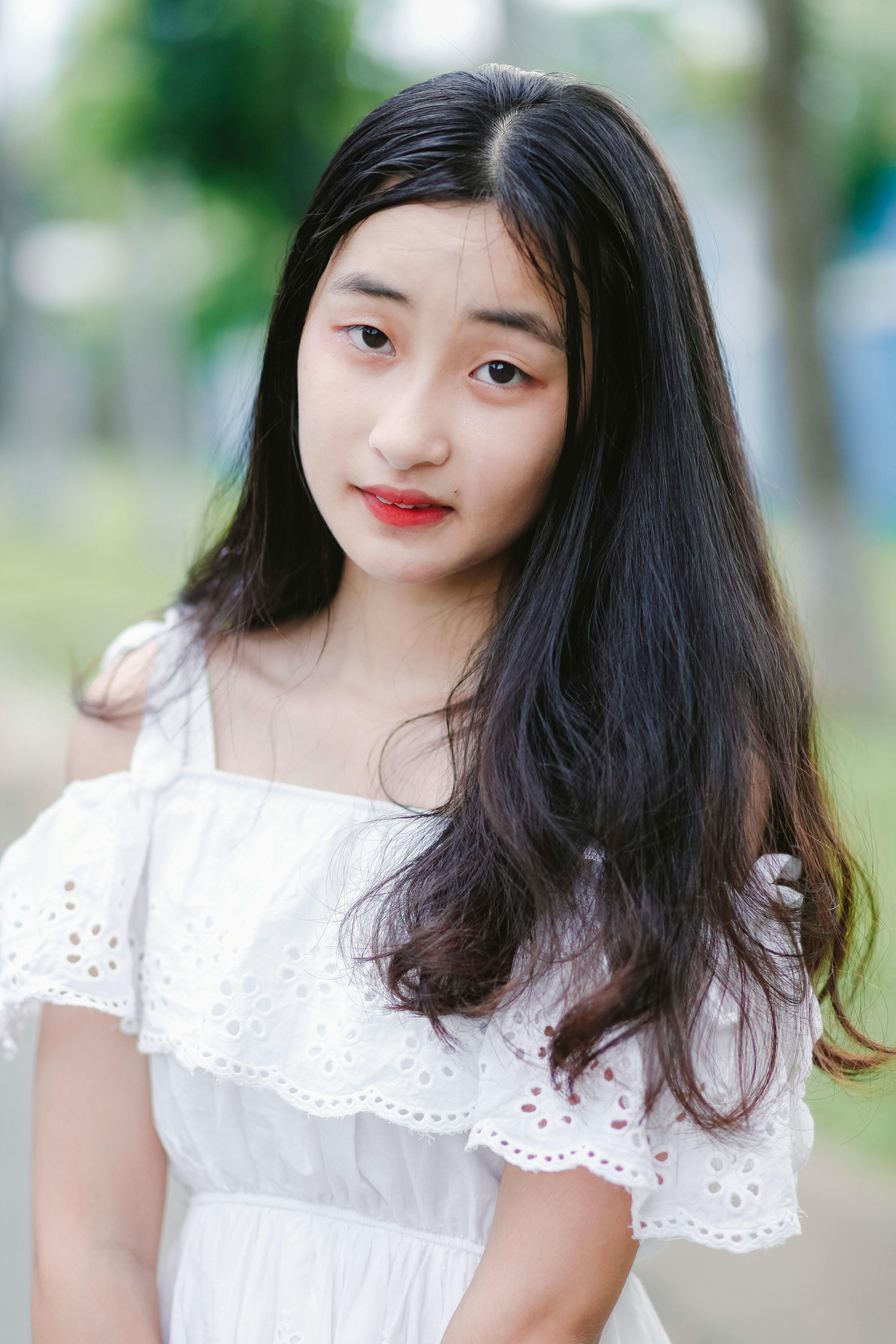 Portrait of a young woman in a white dress, posing outdoors with natural light.