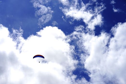 A paraglider soars through a bright blue sky filled with white clouds, capturing the essence of freedom and adventure.