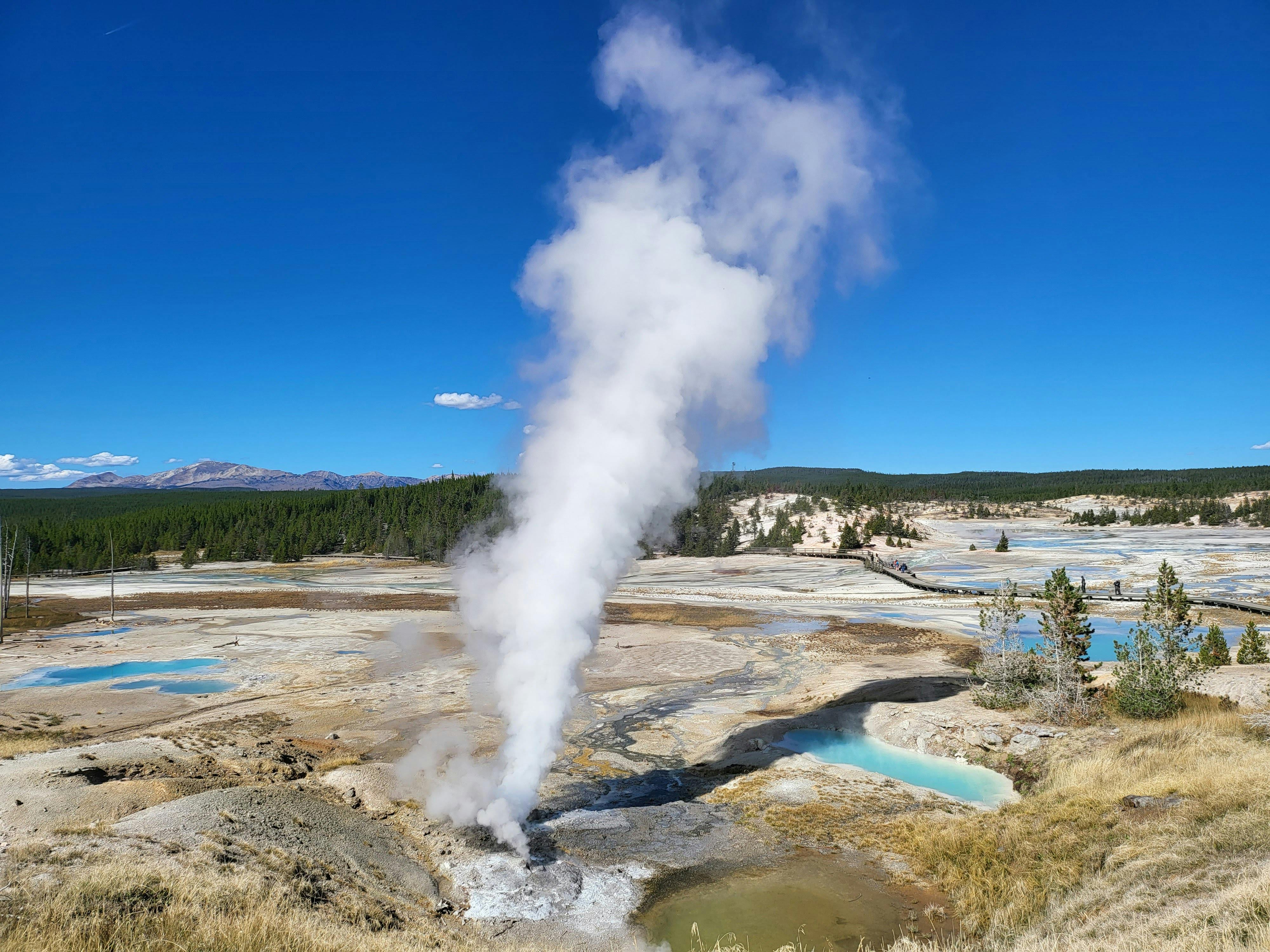An aerial view of Norris Geyser Basin in Yellowstone National Park with steam rising under a clear blue sky.