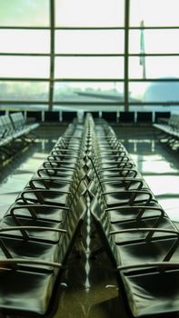 A perspective view of empty seats in a modern airport terminal lounge with large windows.