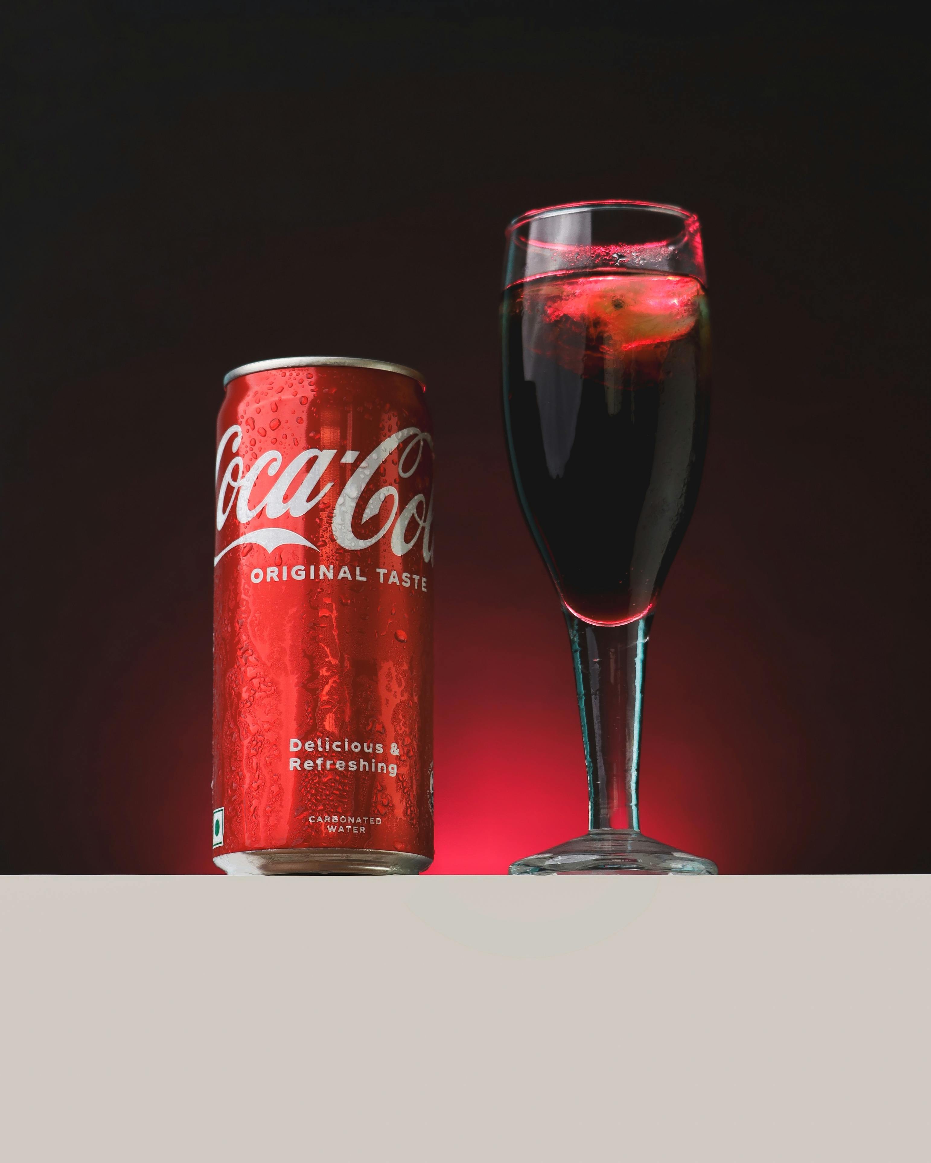 A refreshing Coca-Cola can next to a glass, set against a red background, capturing the drink's allure.