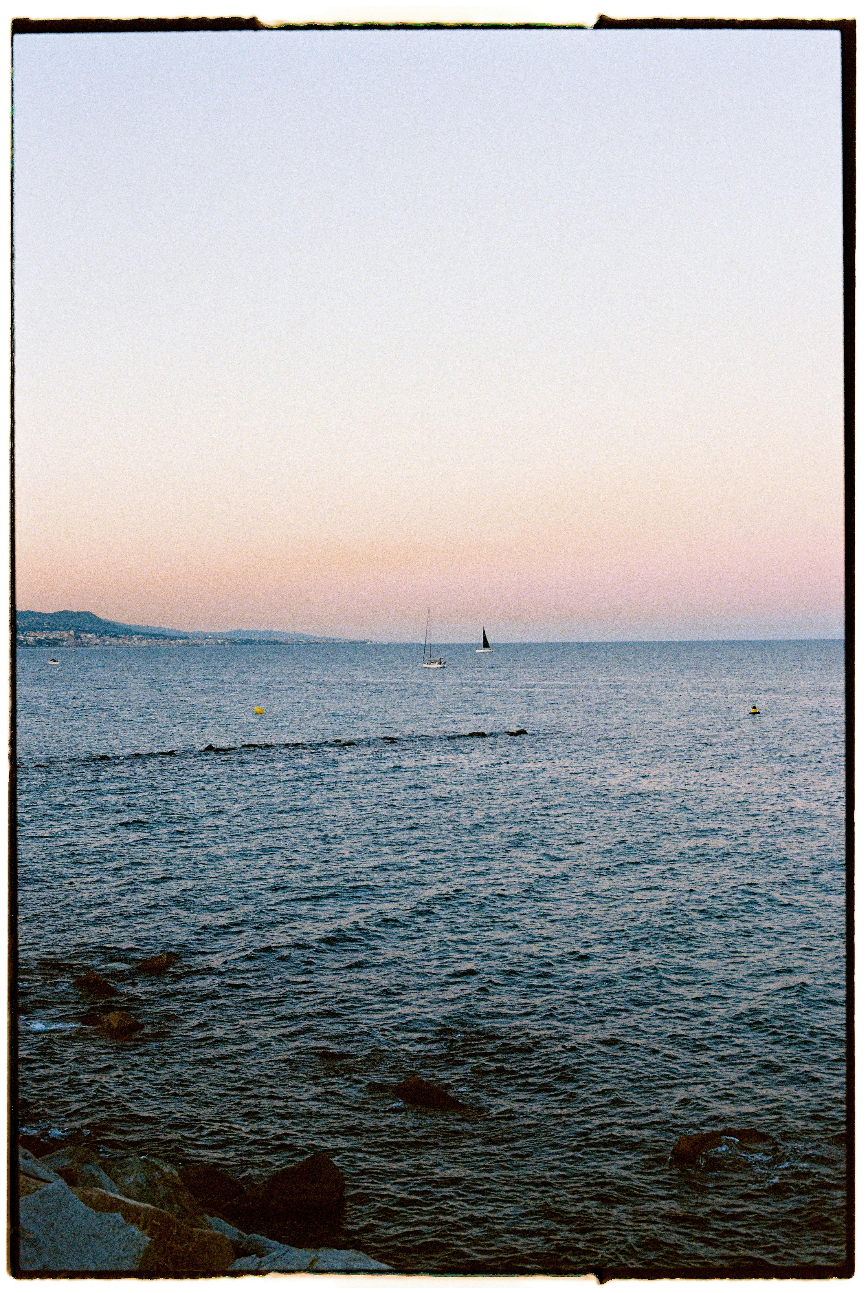 Calm ocean view with distant sailboats and a soft sunset sky over the horizon.