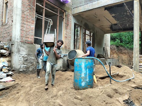 Workers at a construction site carrying materials with a portable concrete mixer in action.