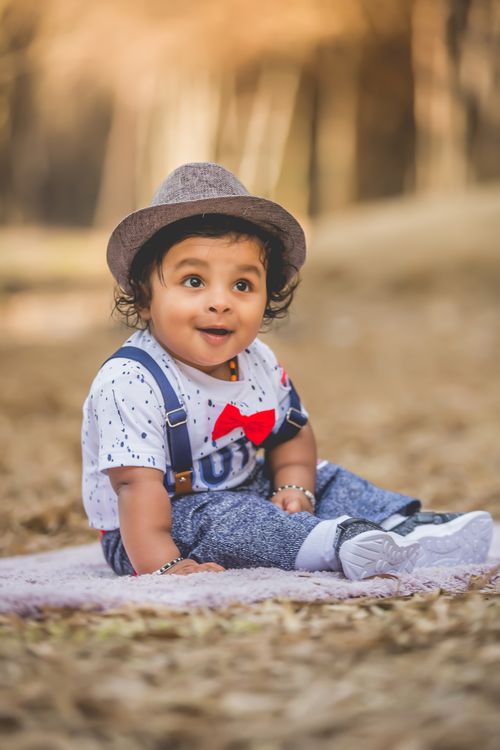 Free Adorable baby boy in a stylish hat sits on a blanket outdoors, embracing innocence and joy. Stock Photo