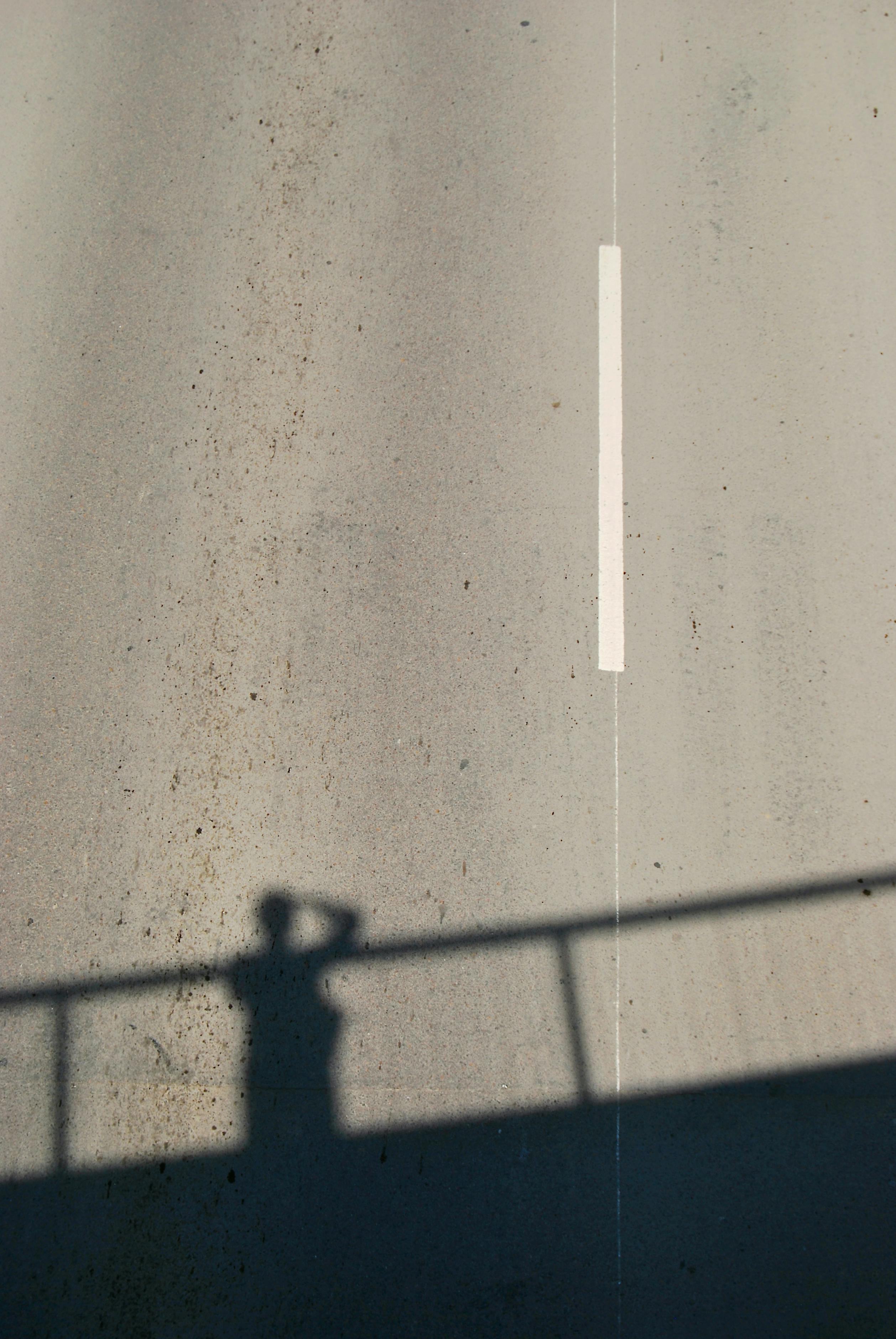 Minimalist shadow of a person on a city street captured from above, highlighting urban solitude.