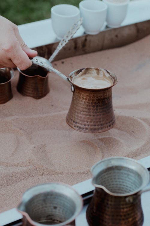 A person pouring coffee into a cup on a sand dune