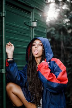 Trendy woman with braided hair and colorful hoodie striking a playful pose outdoors.