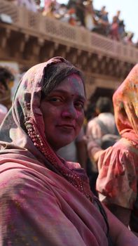 Close-up portrait of a woman covered in colorful powder at a Holi festival outdoors.