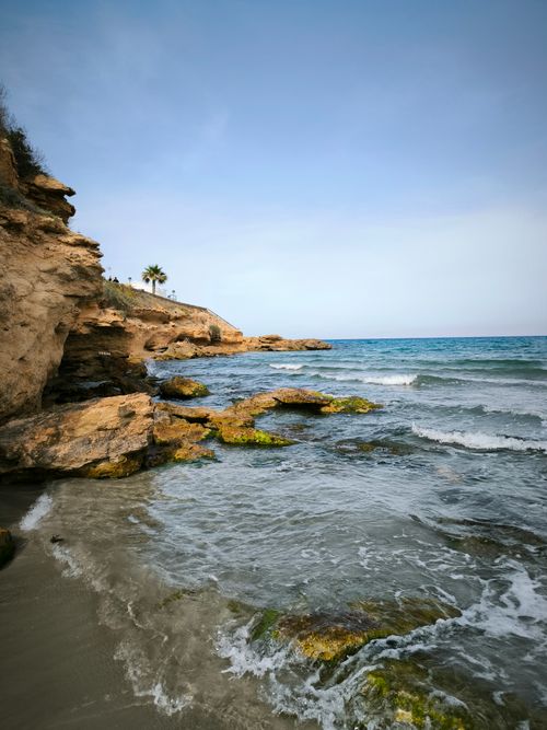 Free A tranquil view of a rocky coastline with gentle waves under a clear sky. Stock Photo