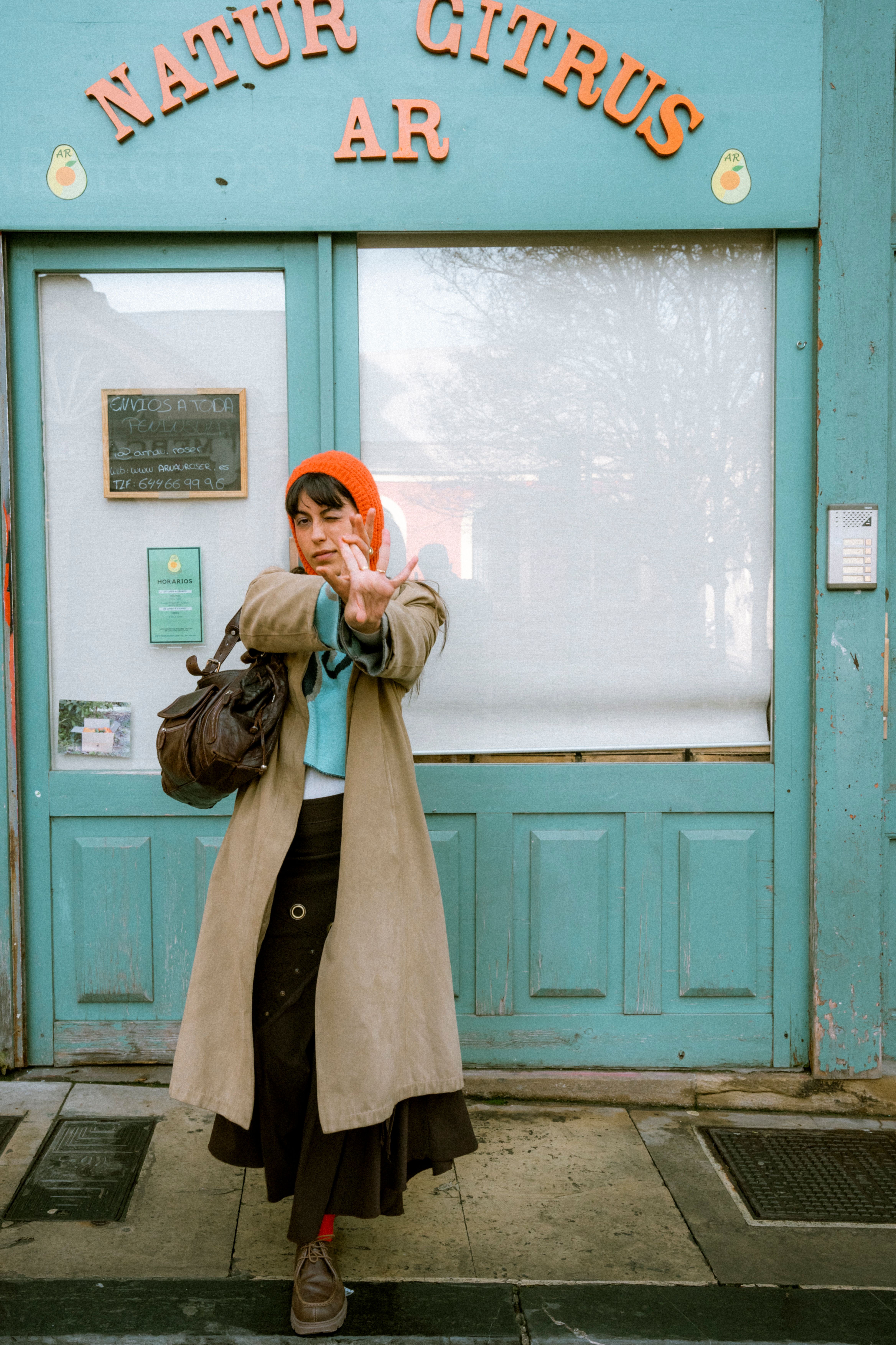 Stylish woman in urban environment posing in front of a rustic blue door labeled 'Natur Citrus AR'.