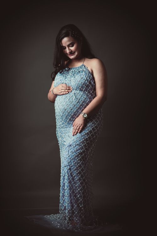 Free Pregnant woman in a blue dress posing elegantly in a studio setting. Stock Photo