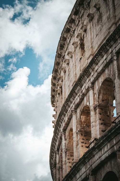 Free A stunning vertical shot of the ancient Roman Colosseum set against a vibrant blue sky with clouds. Stock Photo