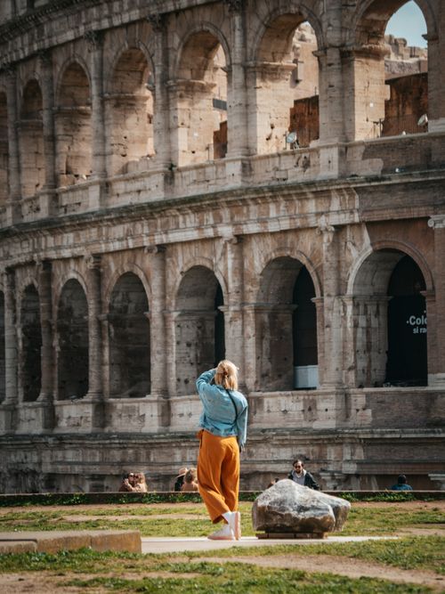 Free A woman photographing the iconic Colosseum, a landmark in Rome, Italy, on a sunny day. Stock Photo