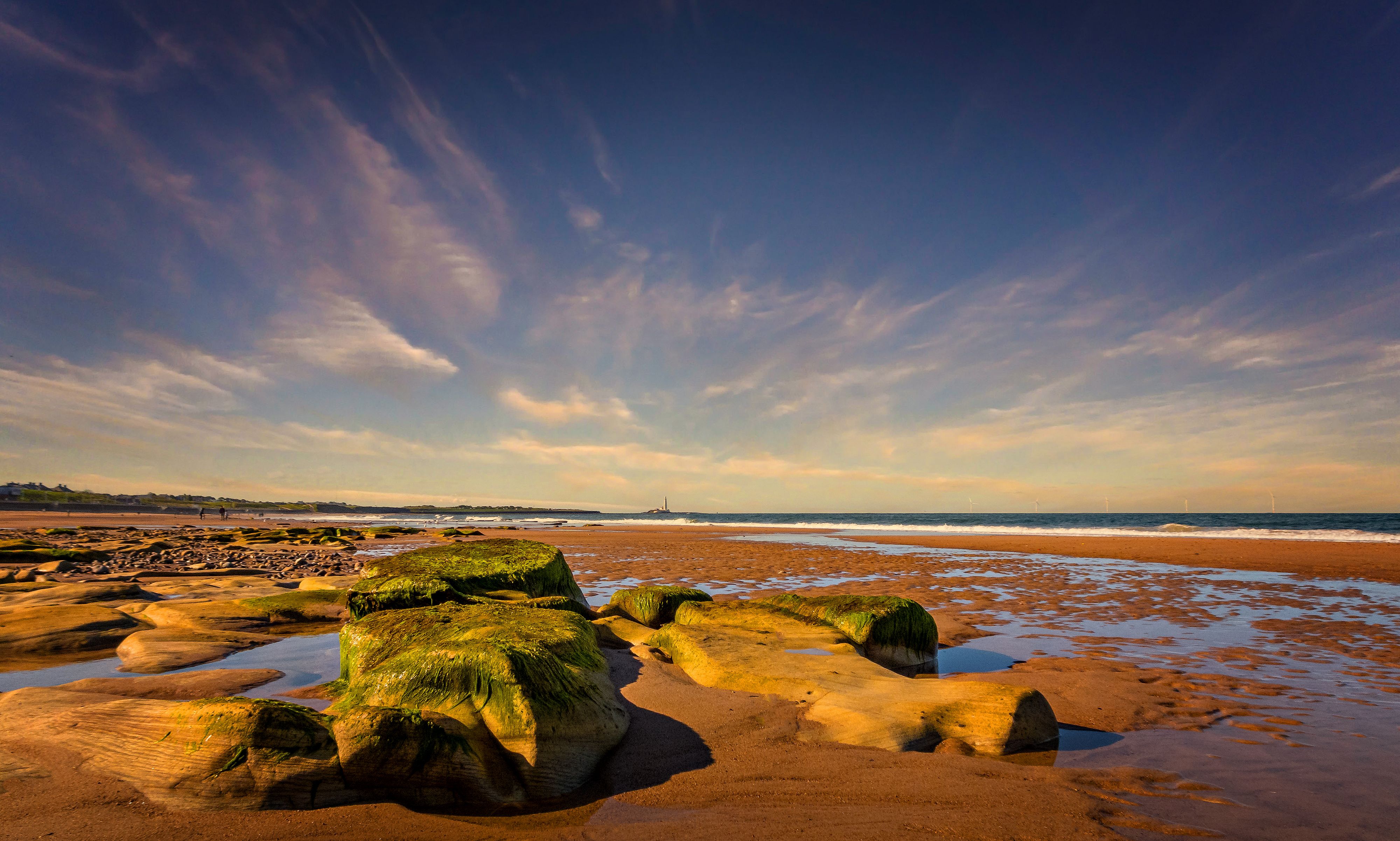 A sandy beach with rocks and a cloudy sky · Free Stock Photo