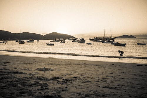 A black and white photo of a beach with boats