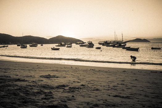 A tranquil beach view with boats, mountains, and a lone person during sunset.