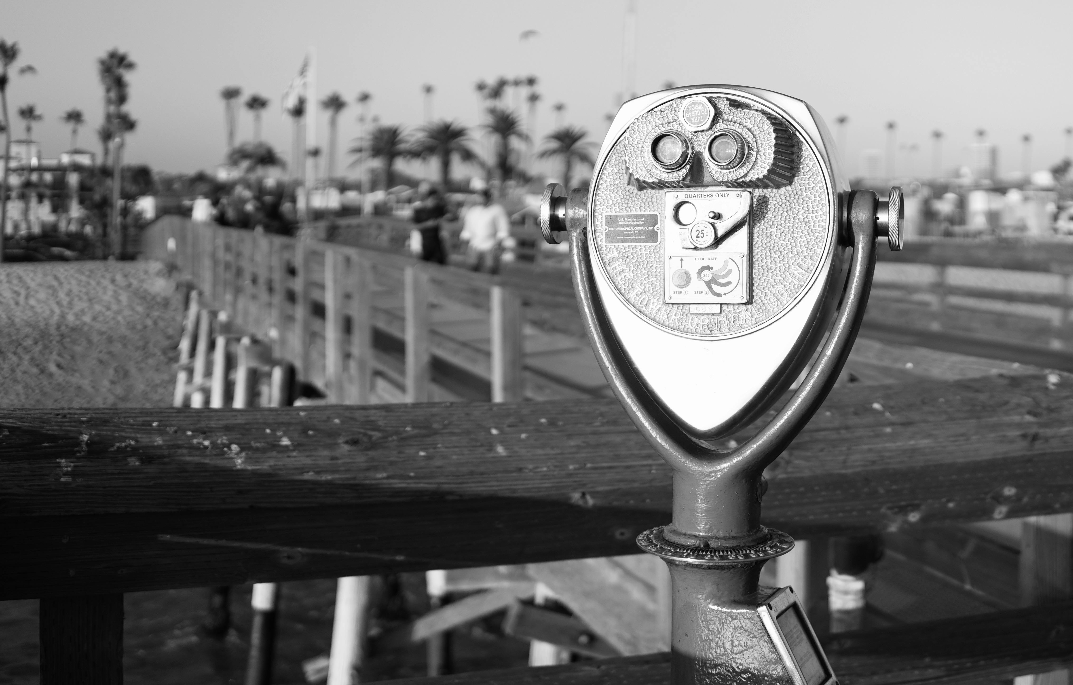 Monochrome viewfinder on a wooden pier overlooking a busy beach scene.