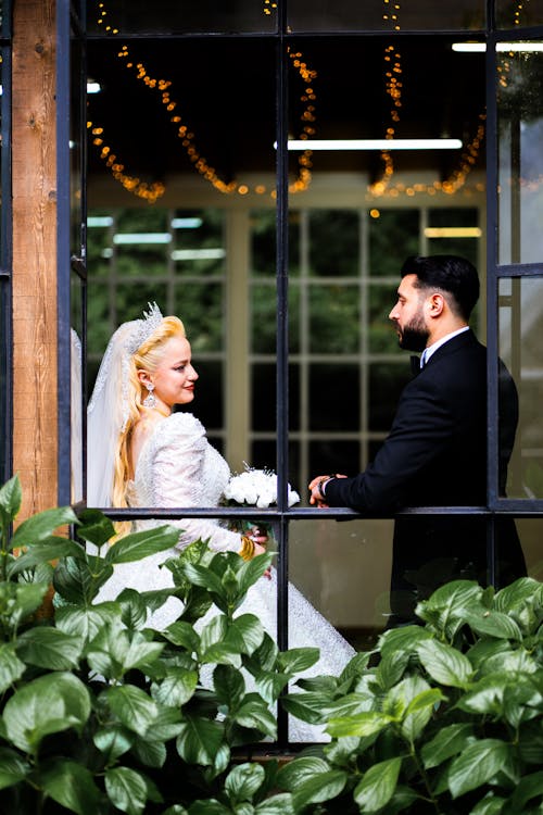 A bride and groom standing in front of a window