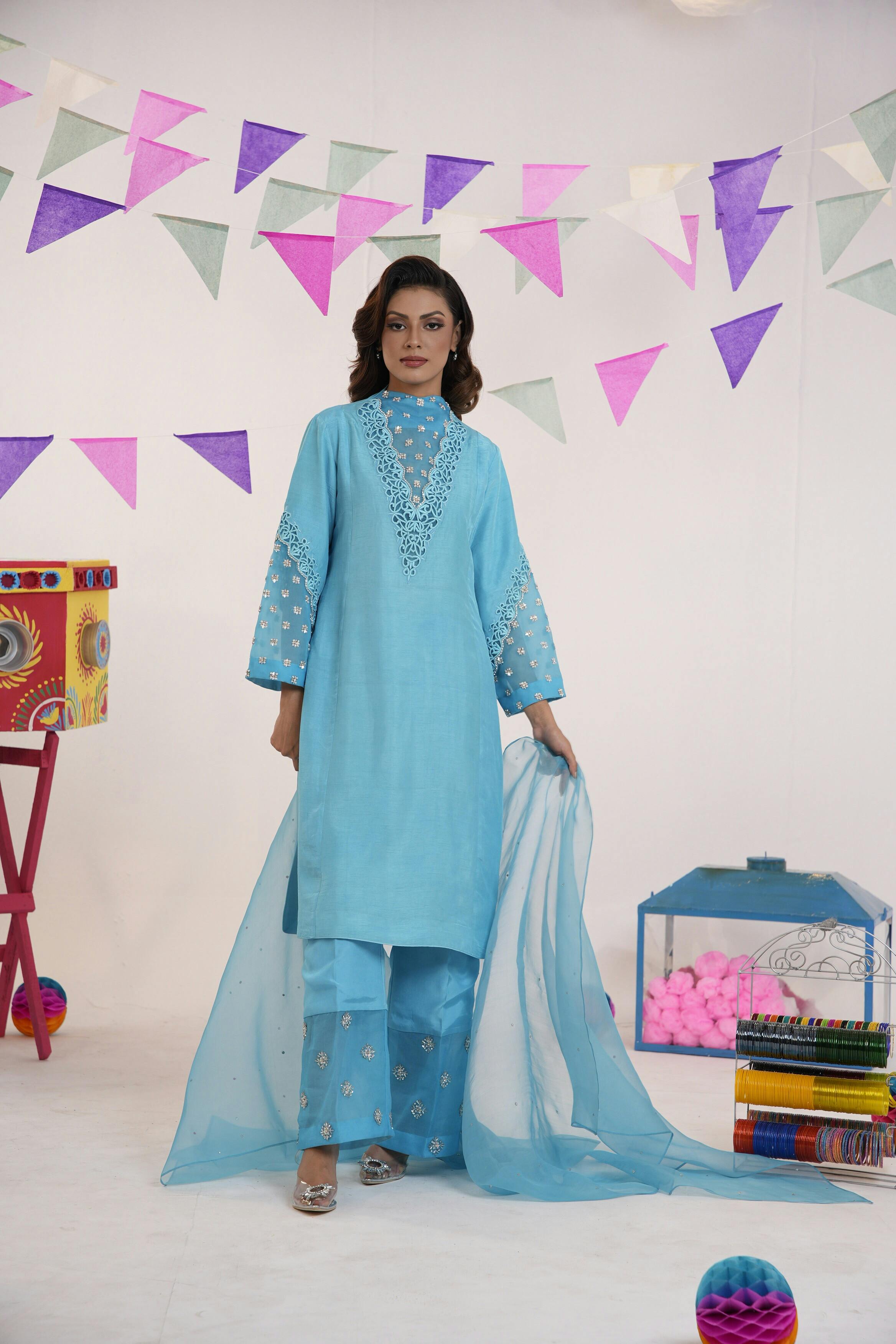 A woman models in traditional blue clothing with vibrant decor in a studio setting.