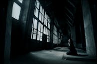 在一座令人毛骨悚然的废弃建筑内，一个独立的人物跪地祈祷，这一幕令人难以忘怀