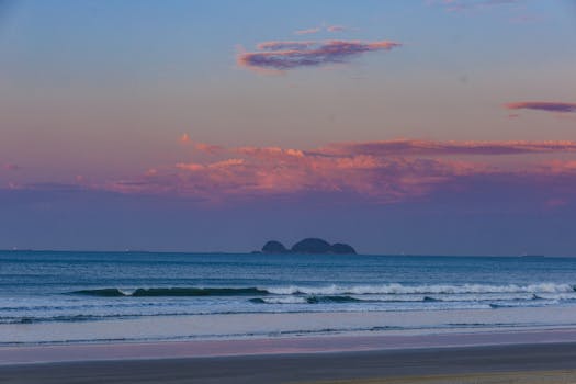 Serene beach scene with pink clouds and gentle waves at sunset.