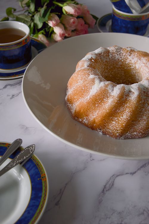 Free Delicious bundt cake dusted with powdered sugar on a marble table with elegant blue tea set. Stock Photo