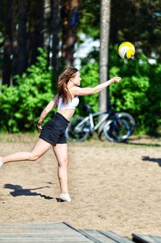 A young woman enjoying beach volleyball in summer with lush greenery in the background.