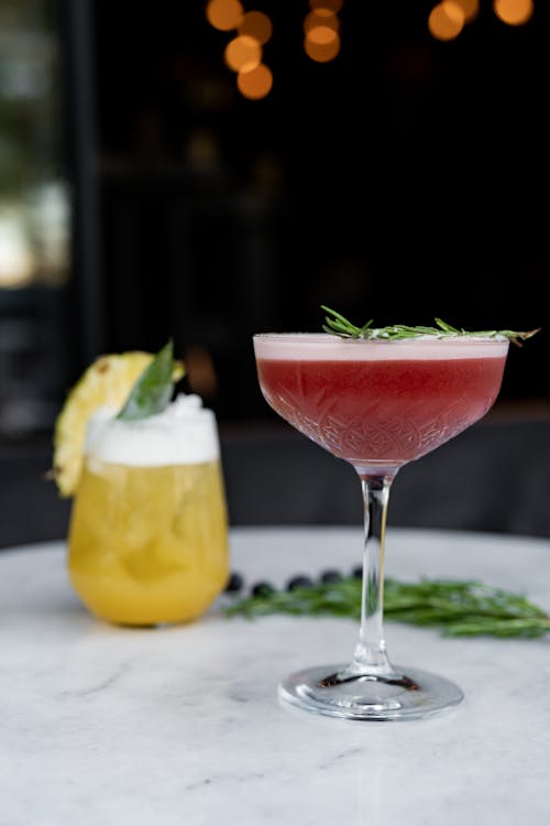 Two cocktails sit on a table with a garnish
