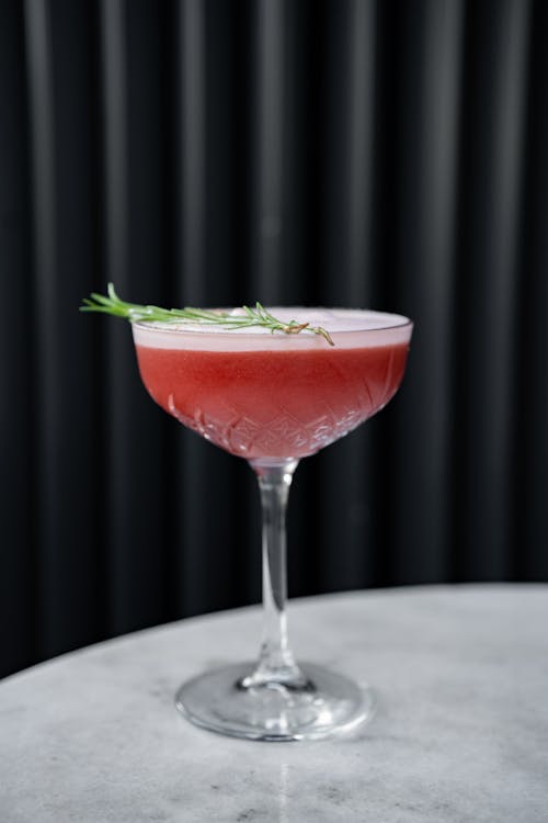 A cocktail with rosemary garnish on a white table