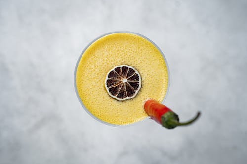 A yellow drink with a chili pepper on top