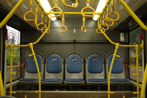 Free Photo of an empty urban bus interior showcasing blue seats and yellow handholds, ideal for public transport themes. Stock Photo