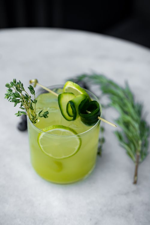 Free A refreshing green cocktail garnished with cucumber, thyme, and lime on a marble table. Stock Photo