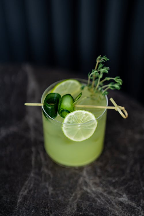 A green cocktail with lime and herbs on a black table