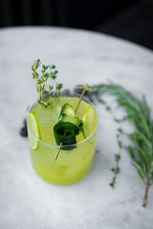 Free Vibrant green mocktail garnished with cucumber slices and herbs on a marble table. Stock Photo