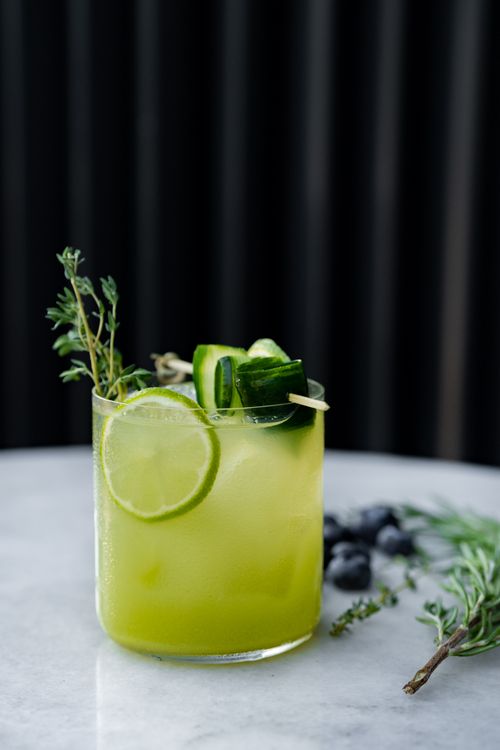 Free Chilled lime and cucumber cocktail garnished with herbs on a marble table, perfect for summer refreshment. Stock Photo