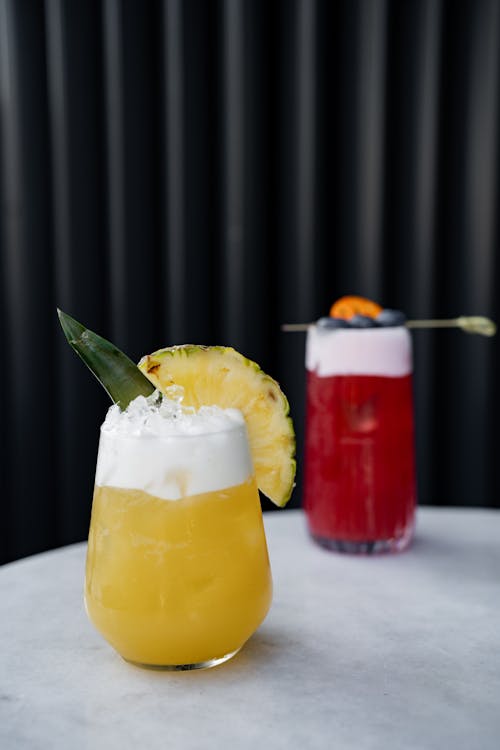 Two cocktails with fruit and pineapple on top